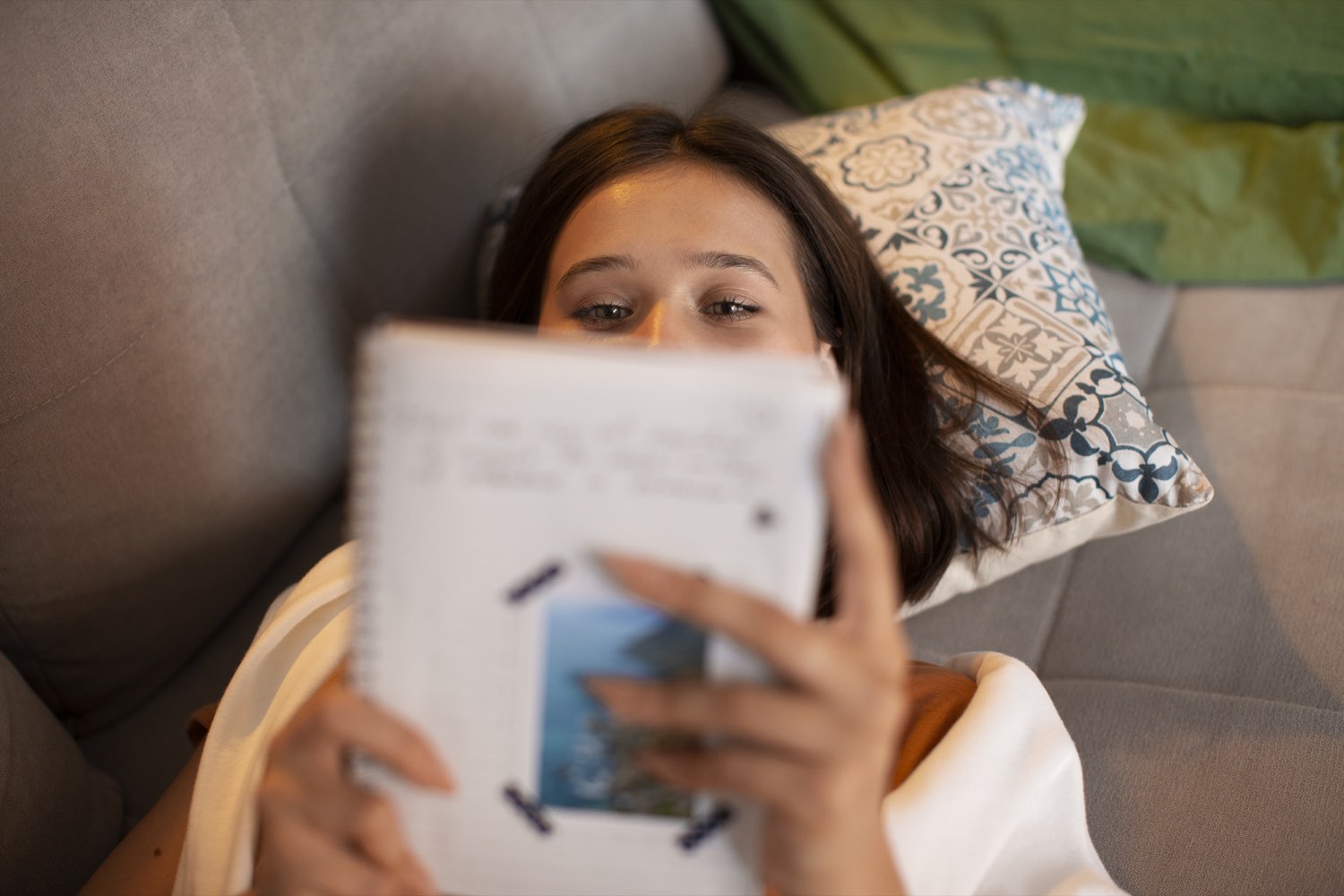 Woman writing in a journal while resting on a sofa.